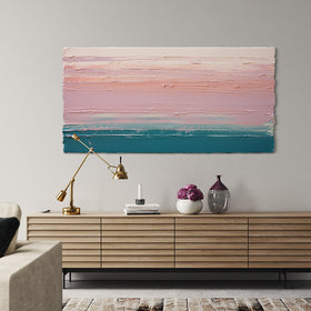 A peach, orange, coral, pale pink and teal thickly textured abstract painting hangs on a wall over a mid century credenza with books, ceramic vase, flowers and a brass contemporary lamp.