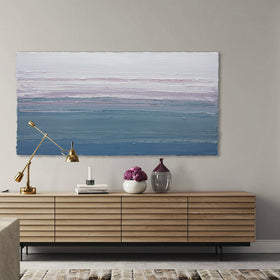 A white, lavender, teal and blue abstract textured painting by Teodora Guererra hangs on a white wall above a natural wood credenza with decorative accessories.
