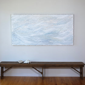 A white and light blue abstract painting with thick, impasto brushstrokes is hung above a bench with seashells.