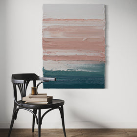 A peach, coral, white and teal with lavender thick textured painting by Teodora Guererra hangs on a white wall in a kitchen with a dark oak chair in front. Sitting on the chair are books and a candle.