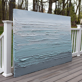 An abstract painting with turquoise impasto brushstrokes in a color gradient is sitting on the artists deck outside.