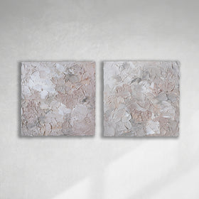 A pair of thickly textured abstract paintings in light pink, grey, coral and white by Teodora Guererra hanging on a white wall.