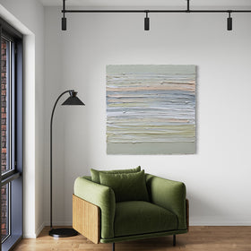 A peach, grey, white, celadon and sage green thickly textured painting by Teodora Guererra hanging on a white wall over a green chair with a black modern floor lamp to the left.