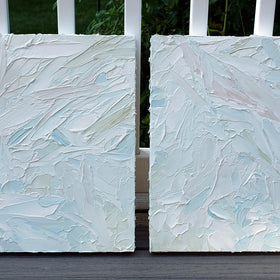 A pair of thickly painted paintings in teal, sea foam green, celadon, white and hints of siena by Teodora Guererra leaning on a deck outside. The two painting are like wall sculptures.