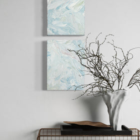 A pair of thickly painted paintings in teal, sea foam green, celadon, white and hints of siena by Teodora Guererra on a white wall over a metal screen table with a white vase and berry branches sitting on the table on a black tray. The two painting are like wall sculptures.