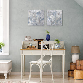 2 paintings hung as a pair shown hanging on the wall over a white table with a plant to the side. The surface of the paintings are decorated with white, blue and grey paint in a thick impasto. Wired and ready to hang.