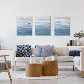 3 paintings are shown hanging on the wall above a cream sectional.. Its surface is decorated with blue and white paint in thick impasto streaks. Wired and ready to hang.
