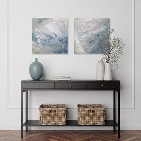 A pair of paintings are hanging on a wall over a dark brown mid century modern table with a sea-foam green vase and books on it. Its surface is decorated with white, blue and green paint in a thick impasto. Wired and ready to hang.