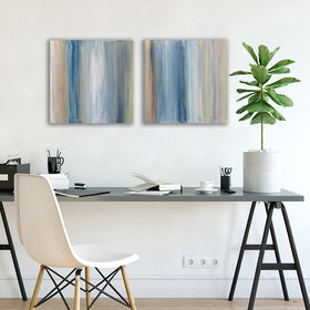 A pair of paintings painted with blue, white, tan and green streaks hangs above a black desk with a plant books, pencils and white chair. Wired and ready to hang.