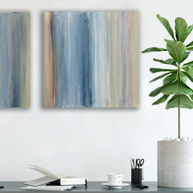 One of a pair of paintings painted with blue, white, tan and green streaks hangs above a black desk with a plant books, pencils and white chair. Wired and ready to hang.
